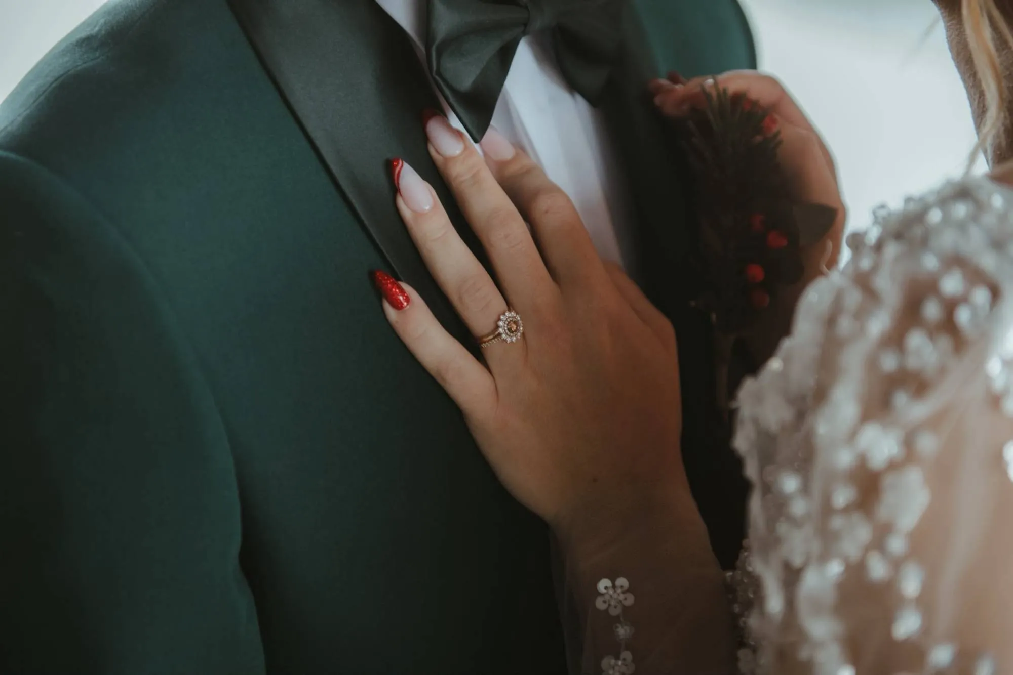 Main de la mariée, bague au doigt, posée sur le revers du costume du marié